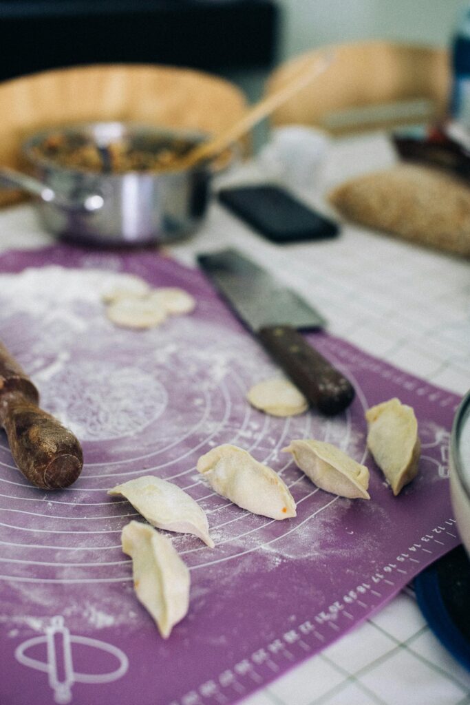 Close-up of homemade dumplings in preparation on a floured surface with kitchen utensils.