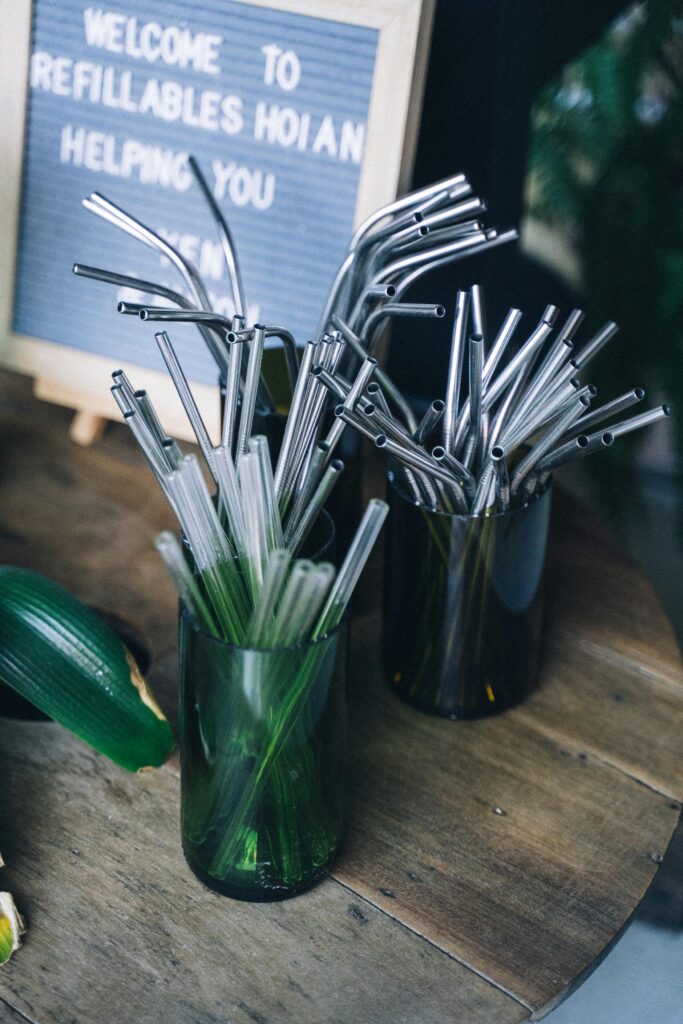 A display of reusable metal and glass straws in green vases, promoting sustainable living.