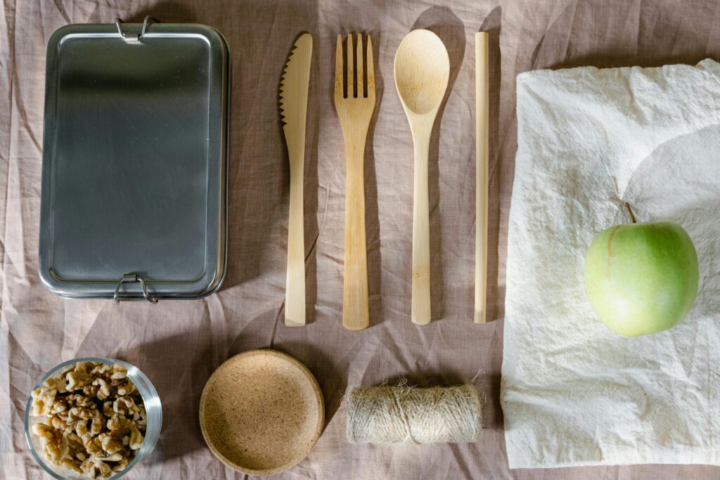 Sustainable flat lay arrangement with wooden utensils, green apple, and lunch box.